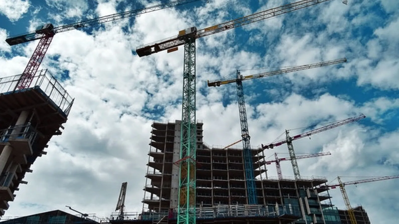 Cranes and building construction against blue sky and white clouds