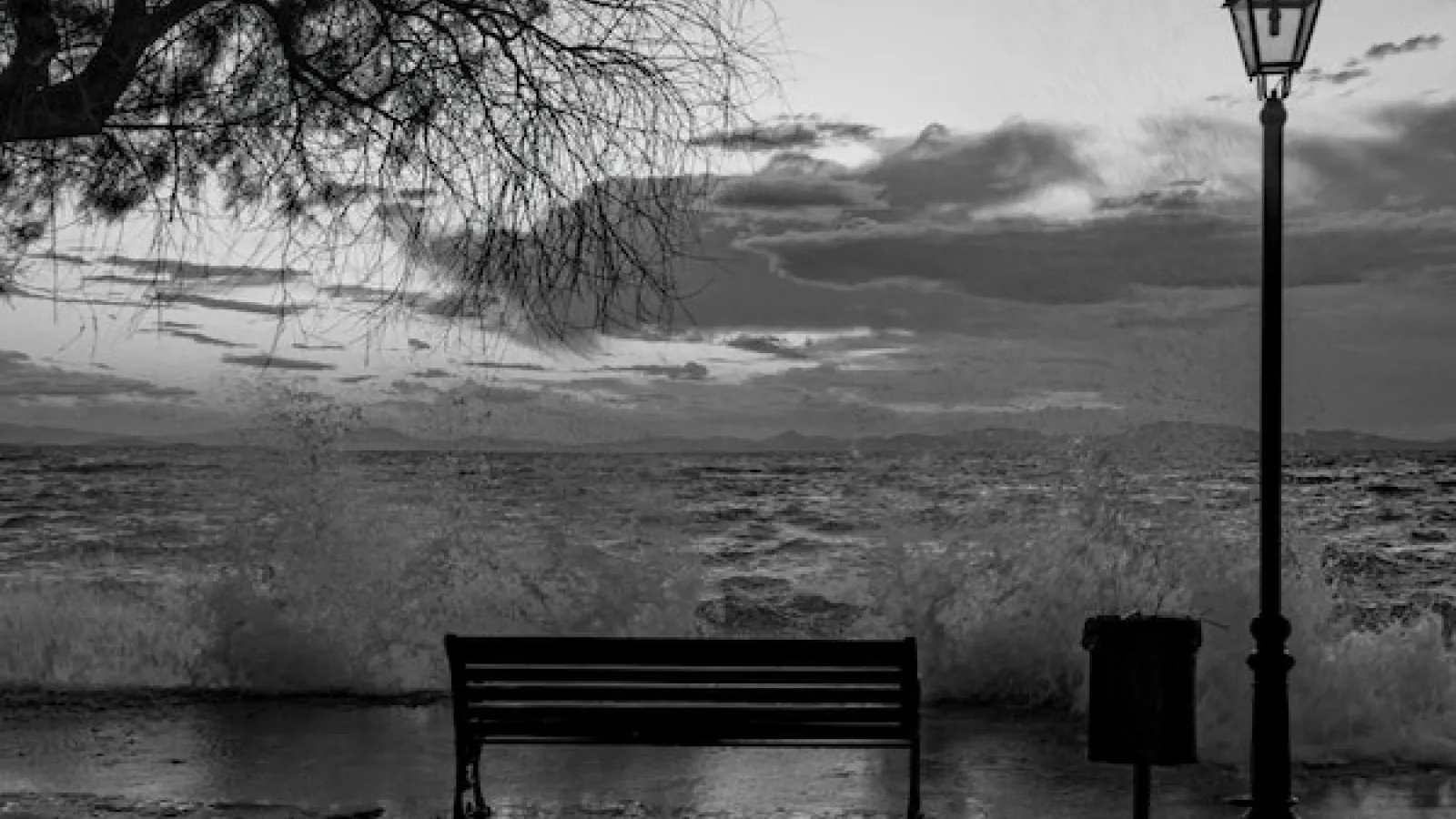 Black and white image of Park bench next to light post facing water getting flooded from water surge