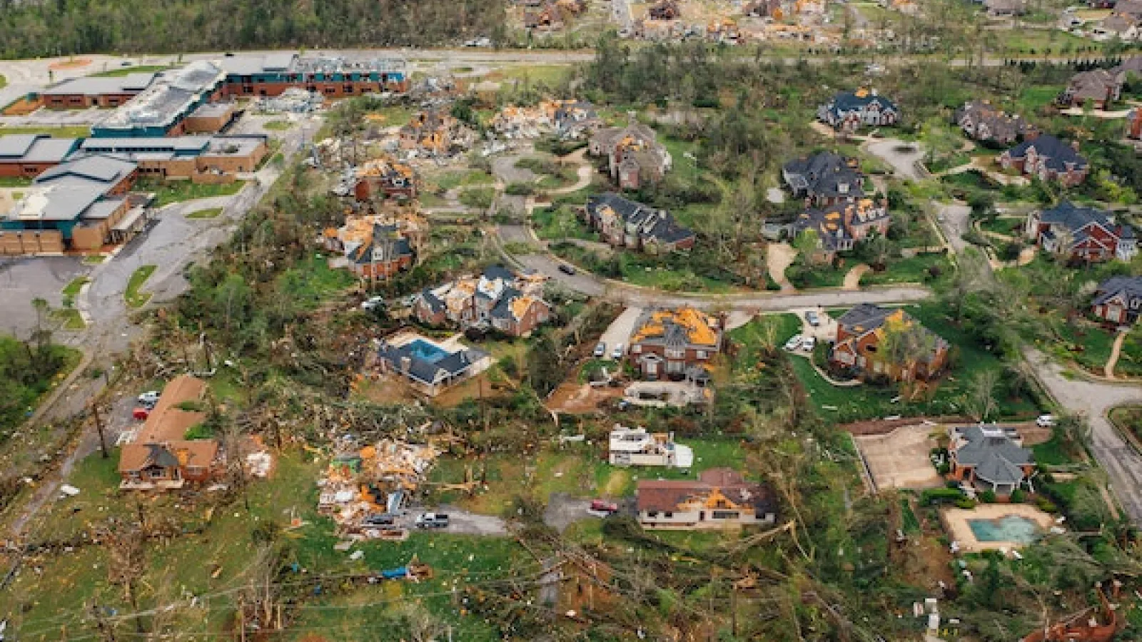 Aerial image of a tornado-stricken subdivision with damaged trees and houses and downed wires