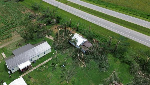 Tornado damage with trees snapped and falling on top of a house.