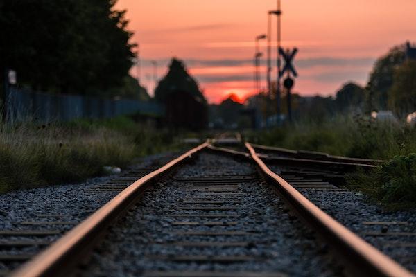 train tracks among green trees and shrubs at sunset