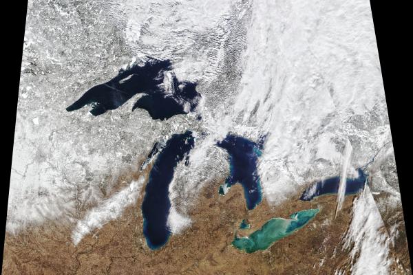 Satellite image of the great lakes with the top half of the image white, covered in snow and the bottom brown and the lakes dark and light blue.. 